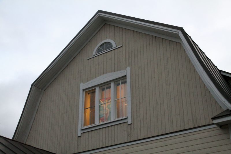 Kuvassa on majatalon ylemmän kerroksen seinä ja ikkuna, josta näkyy sisäpuolelle laitettu lasimaalaus.